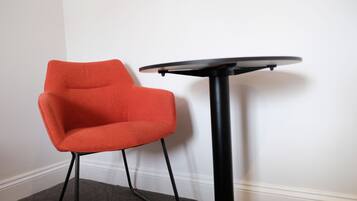 Une chaise rouge et une petite table noire adossées à un mur blanc.
