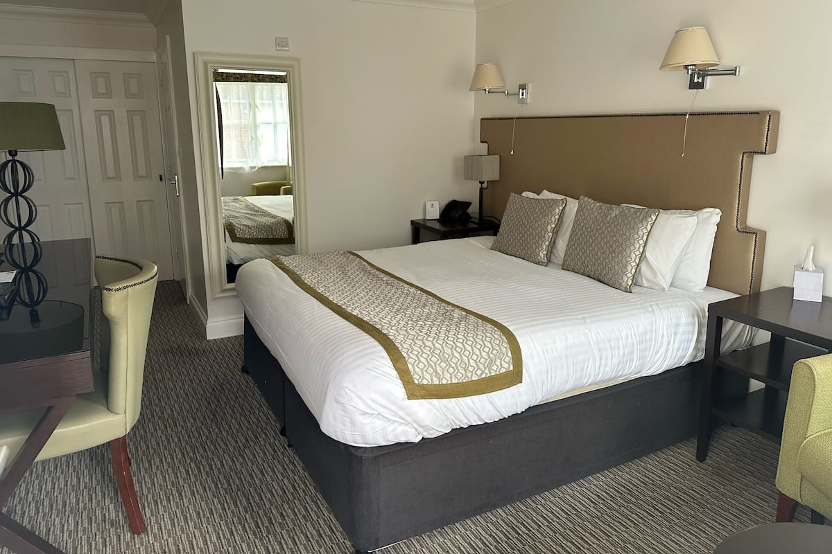 A hotel room with a large bed, bedside tables, a desk, and a mirror.