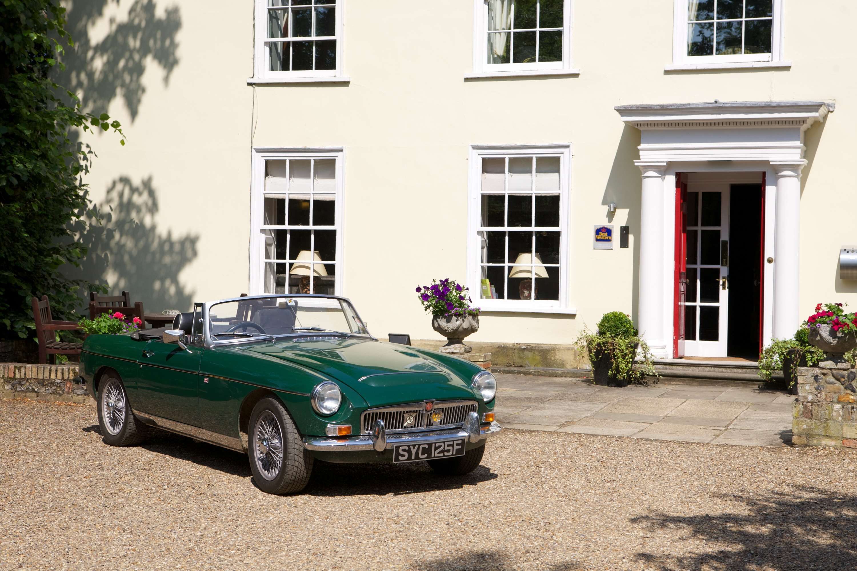 A green convertible car parked in front of a building with white windows and a red door.