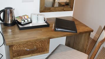 Et træbord med en bærbar computer, en bakke med kaffekopper og en elkedel, en stol og en lille skraldespand.