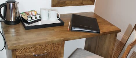 A wooden desk with a laptop, a tray with coffee cups and a kettle, a chair, and a small trash bin.