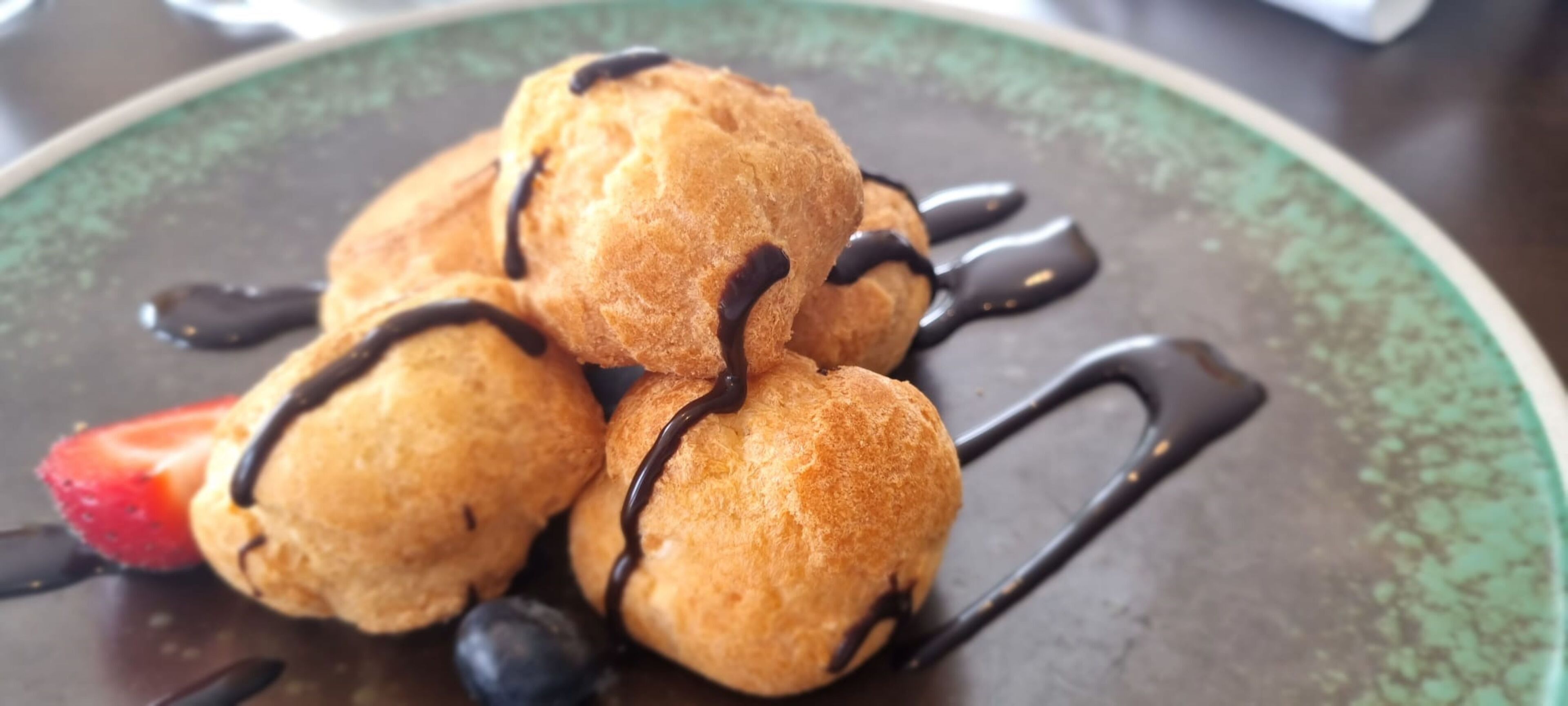 A plate of profiteroles with chocolate sauce and a strawberry.