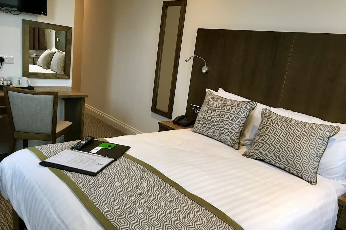 A hotel room with a bed, a desk, a chair, a mirror, and a telephone.