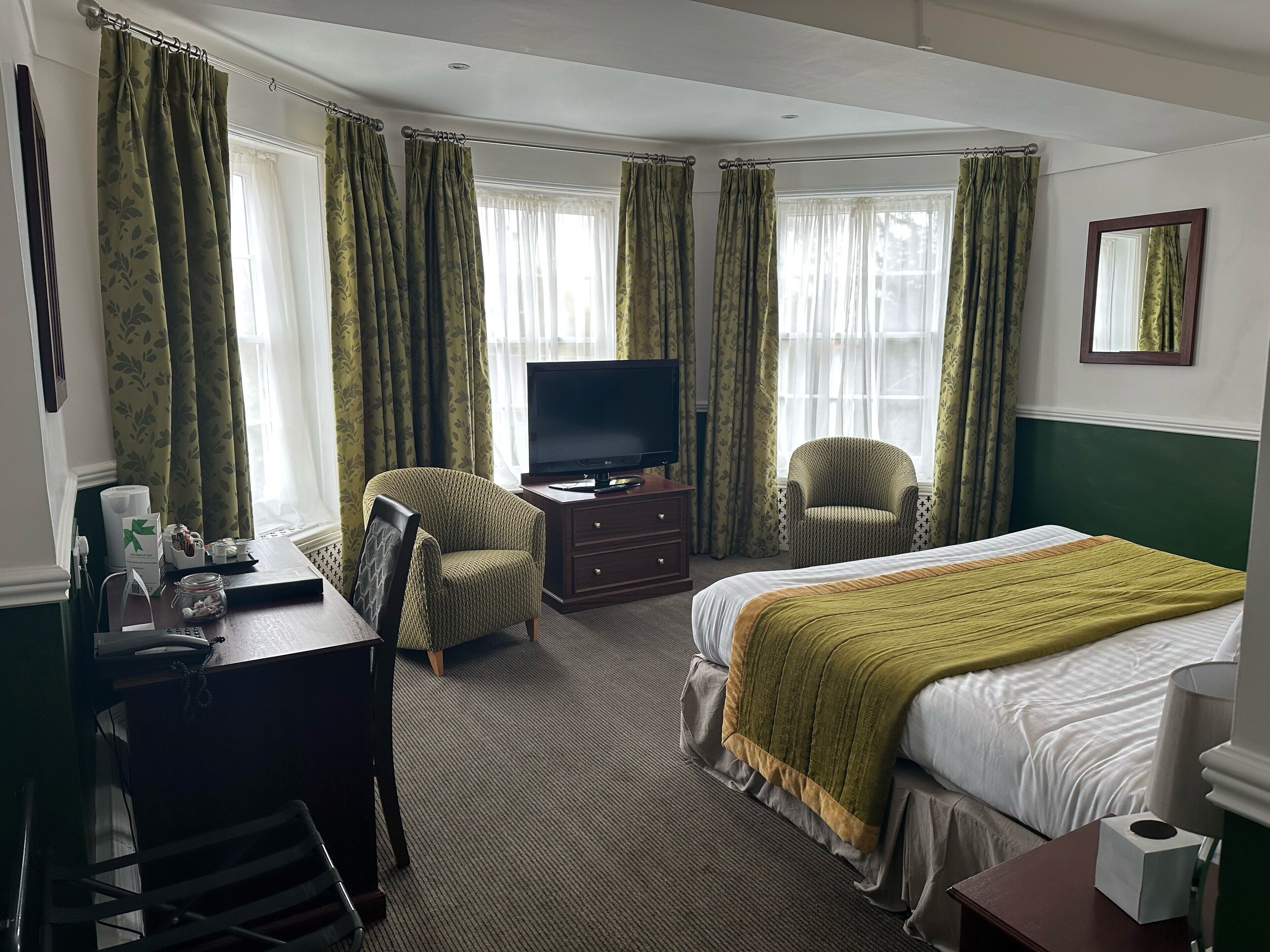 A hotel room with a bed, a desk, a television, two armchairs, and a window with curtains.