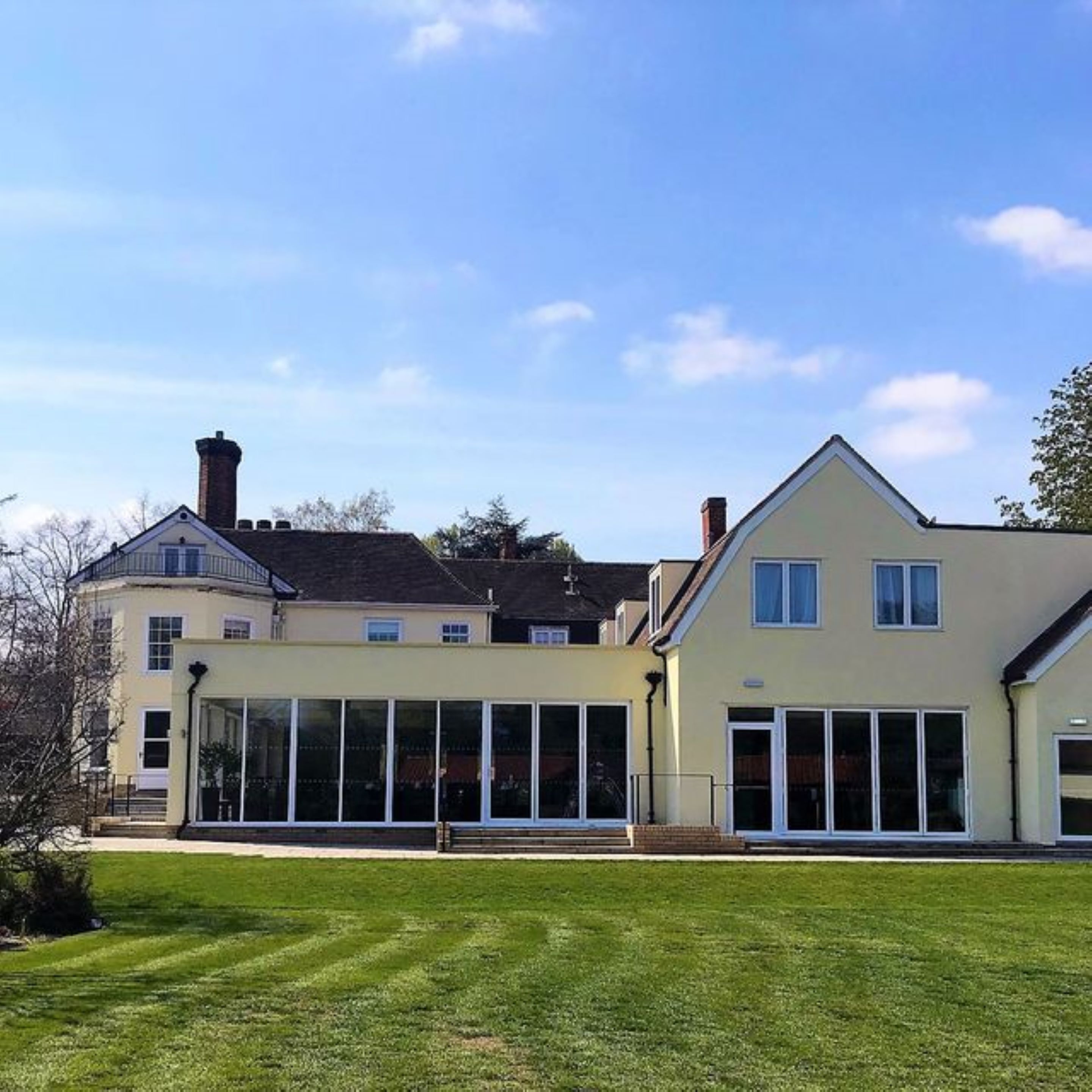 A two-story house with a large glass conservatory, a well-maintained lawn, and a clear blue sky.