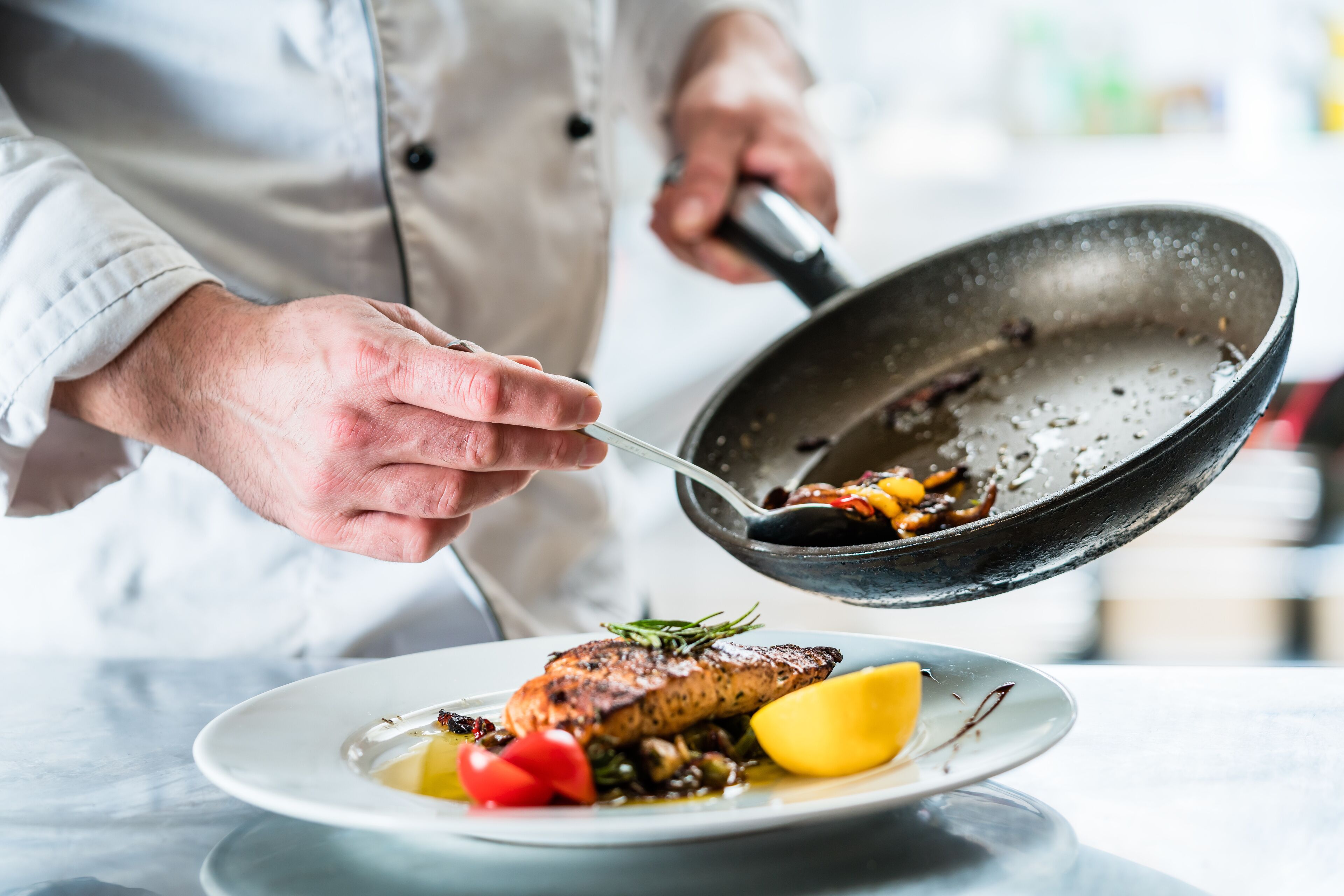 Un chef prépare un filet de poisson avec des légumes sur une assiette.