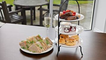 A table with a three-tiered dessert stand, a plate of sandwiches, and a glass of white wine.