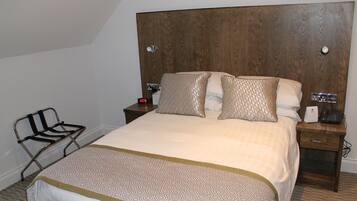 A neatly made bed with patterned bedding, a bedside table with a phone and a lamp, and a chair with a metal frame.