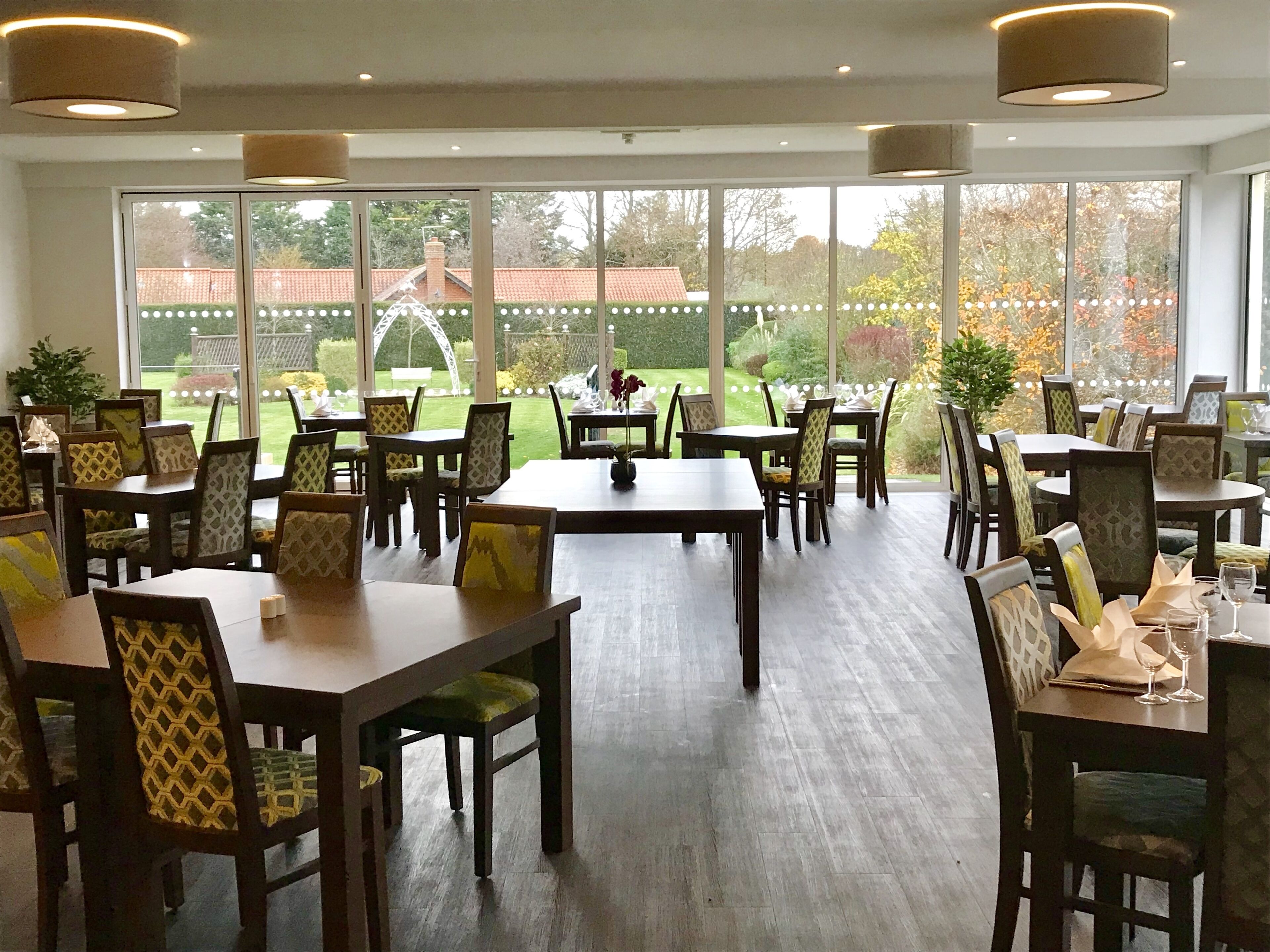 A spacious indoor dining area with multiple tables and chairs, large windows offering a view of the outdoors, and a well-lit ceiling.