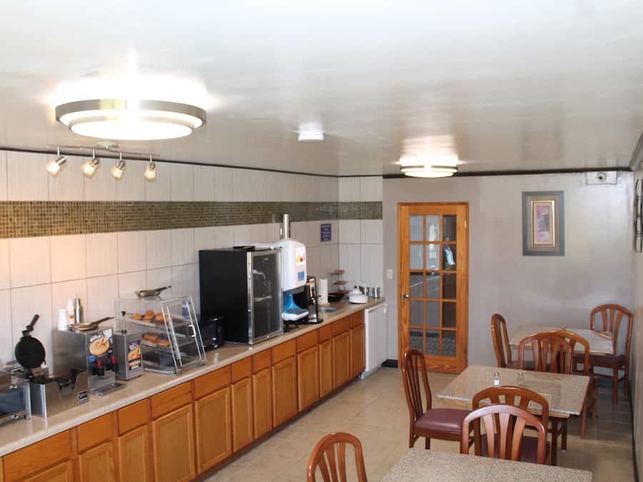 A kitchen with wooden cabinets, a refrigerator, a coffee machine, and a dining area with wooden chairs and tables.