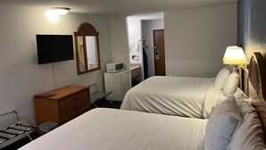 A hotel room with two beds, a TV, a microwave, a dresser, and a bathroom visible through an open door.