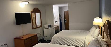 Habitación de hotel con dos camas, televisión, microondas, cómoda y baño visible a través de una puerta abierta.