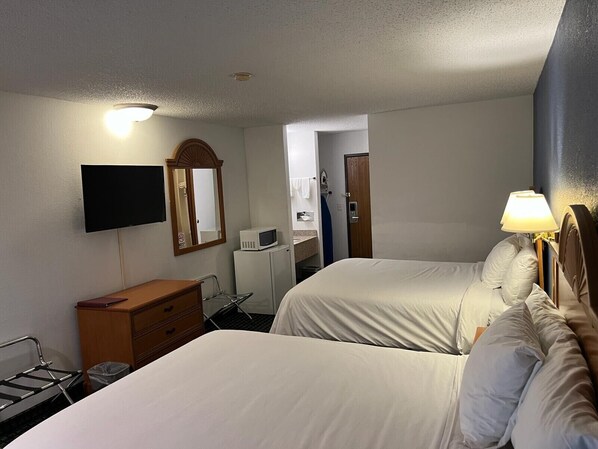 A hotel room with two beds, a TV, a microwave, a dresser, and a bathroom visible through an open door.