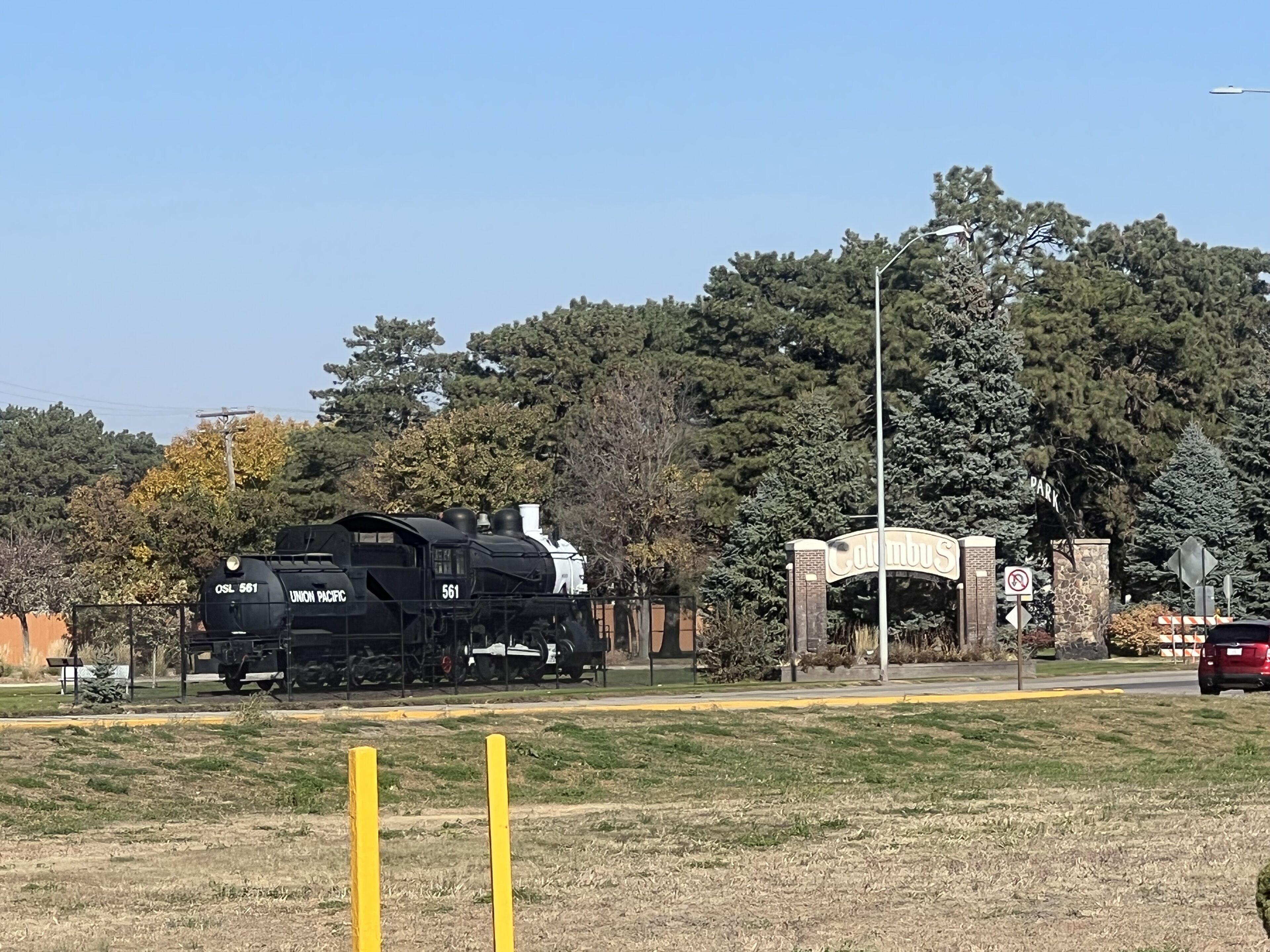 A black Union Pacific train numbered 561 on tracks with a sign for Columbus Park in the background.