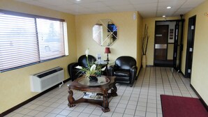 A reception area with a tiled floor, a reception desk, a black leather chair, a potted plant, and a red carpet.