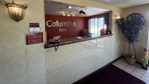 The Columbus Inn reception area with a marble counter, a reception desk, and a large mirror reflecting the interior.