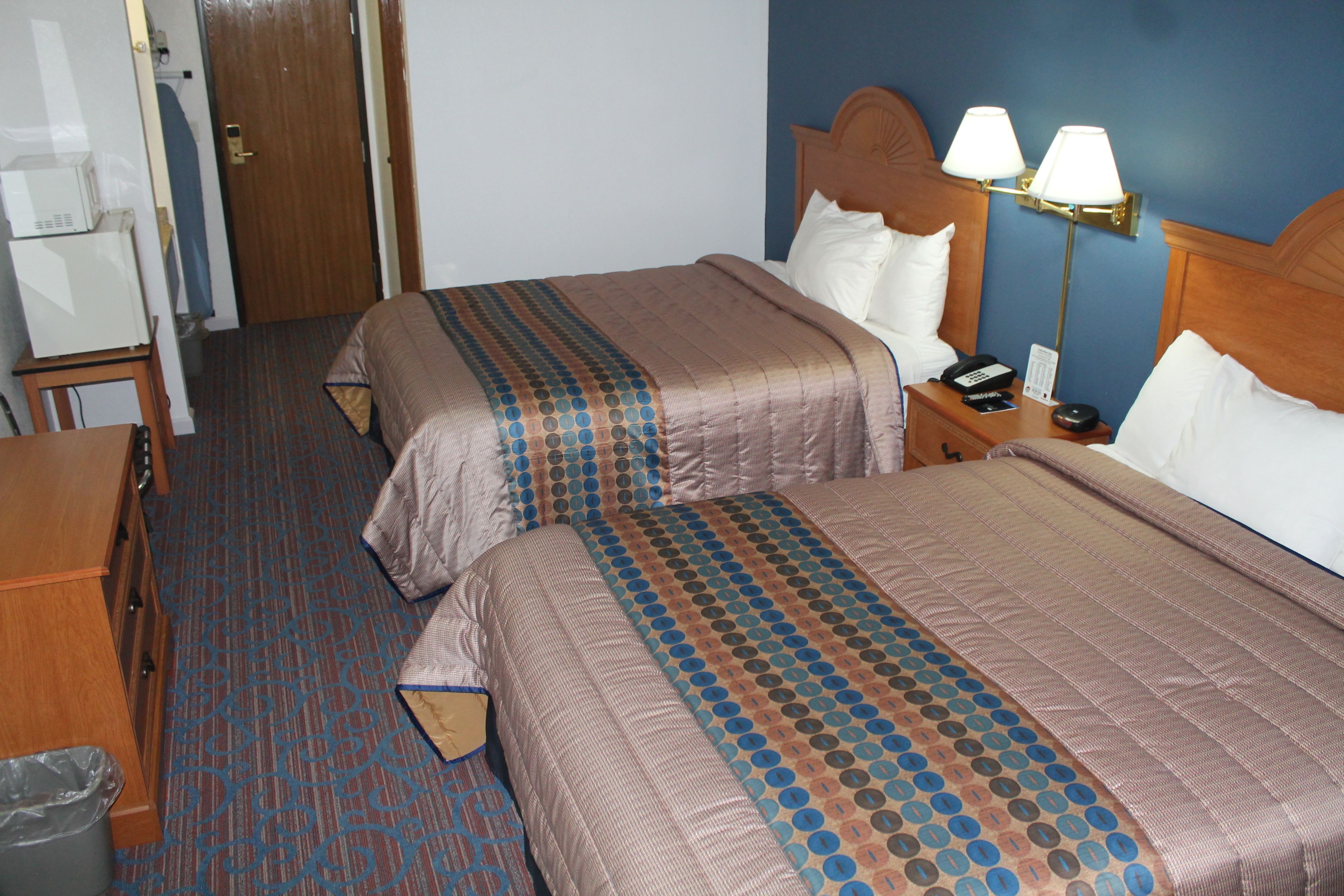A hotel room with two beds, a wooden nightstand, a desk, and a trash bin.