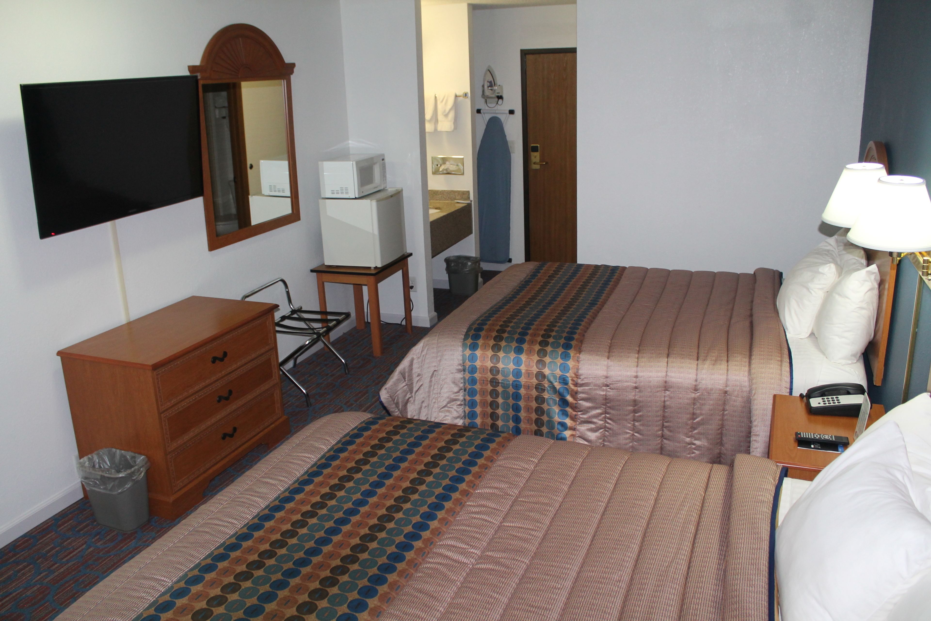 Habitación de hotel con dos camas, un aparador, televisión, microondas, bote de basura y baño visible a través de una puerta abierta.
