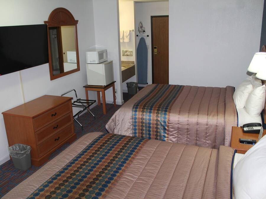 Habitación de hotel con dos camas, un aparador, televisión, microondas, bote de basura y baño visible a través de una puerta abierta.