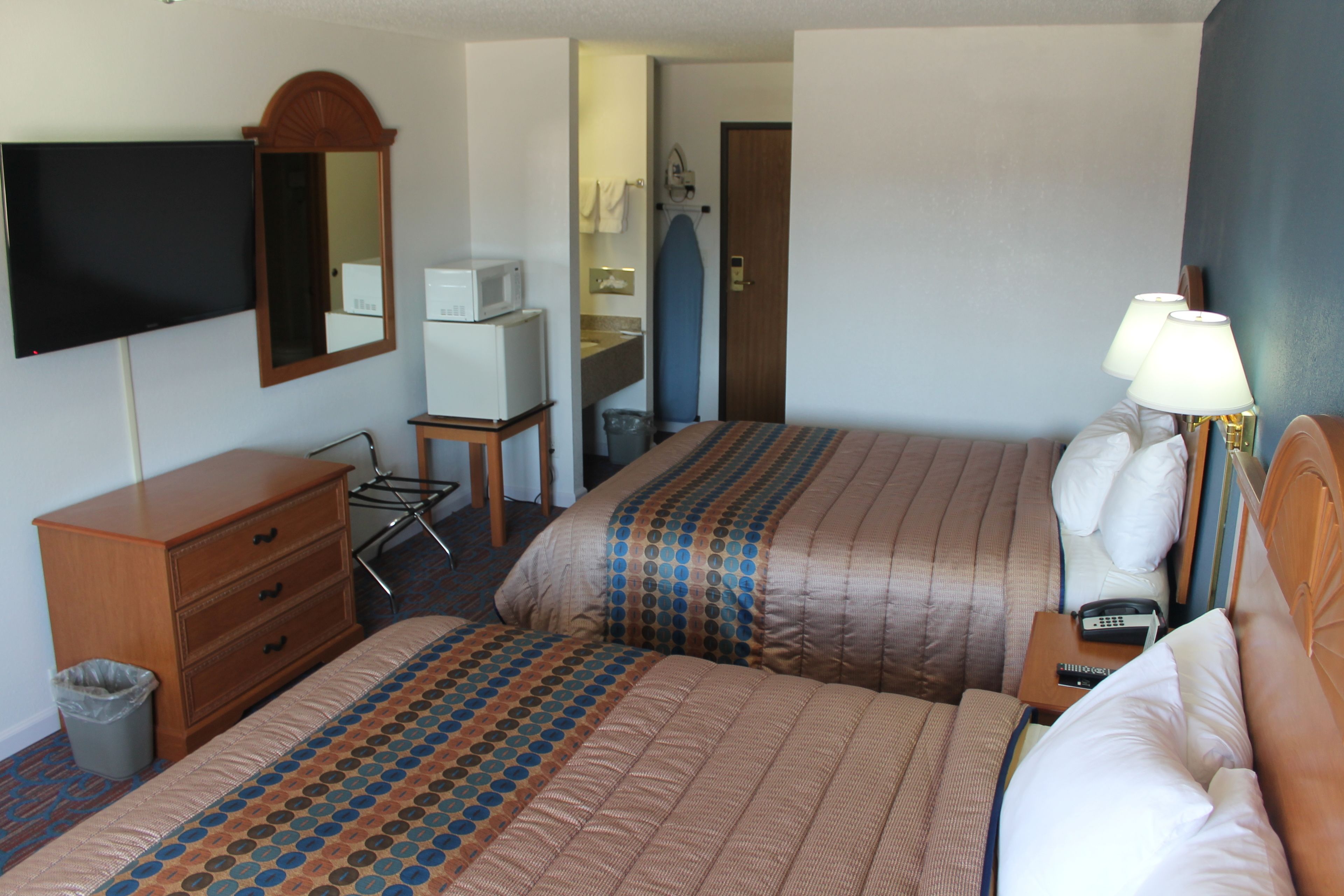 Habitación de hotel con dos camas, televisión, espejo, microondas y una mesita de noche con lámpara.