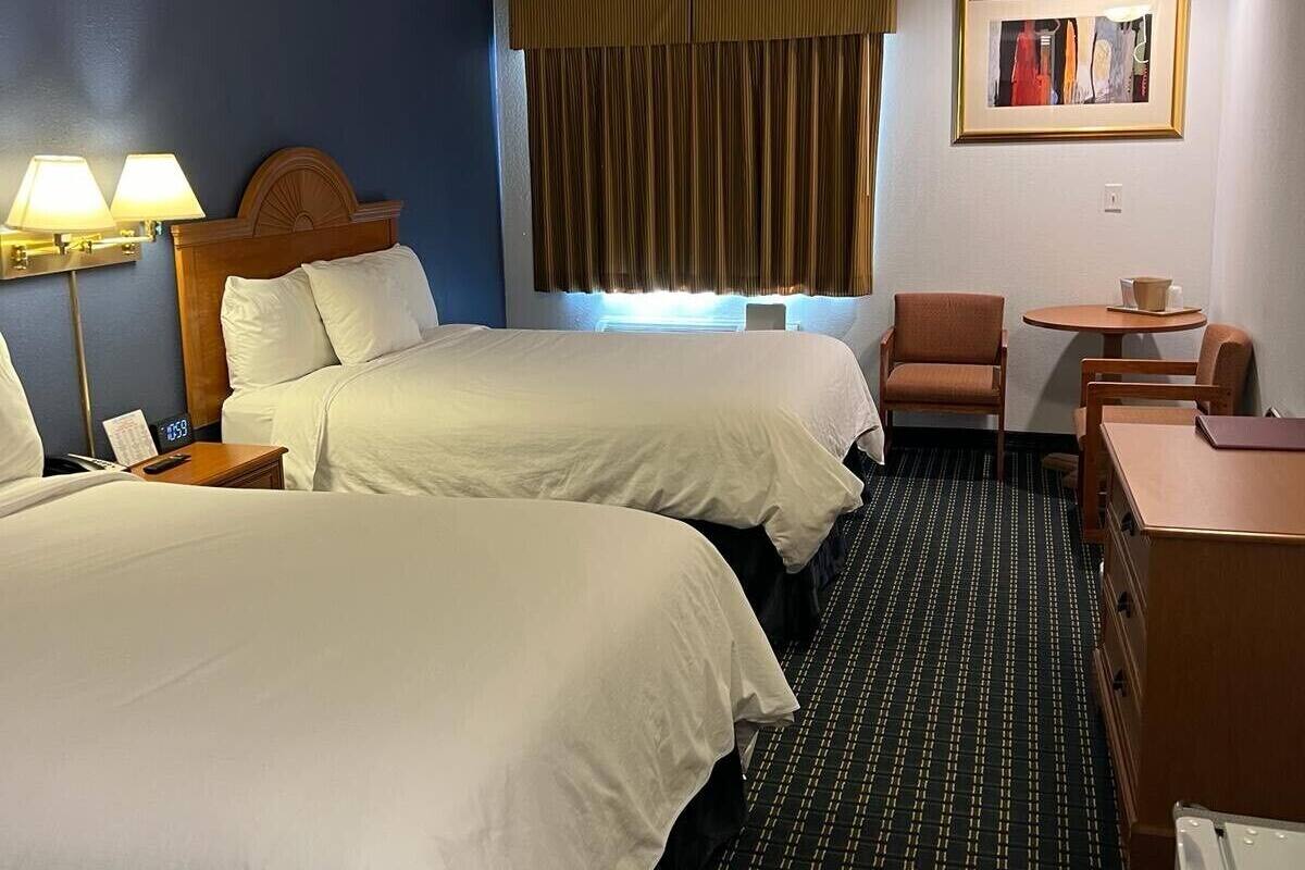 A hotel room with two beds, a desk, a chair, a small table, and a painting on the wall.