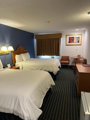 Two single beds with white linens, a desk, and a table with chairs.