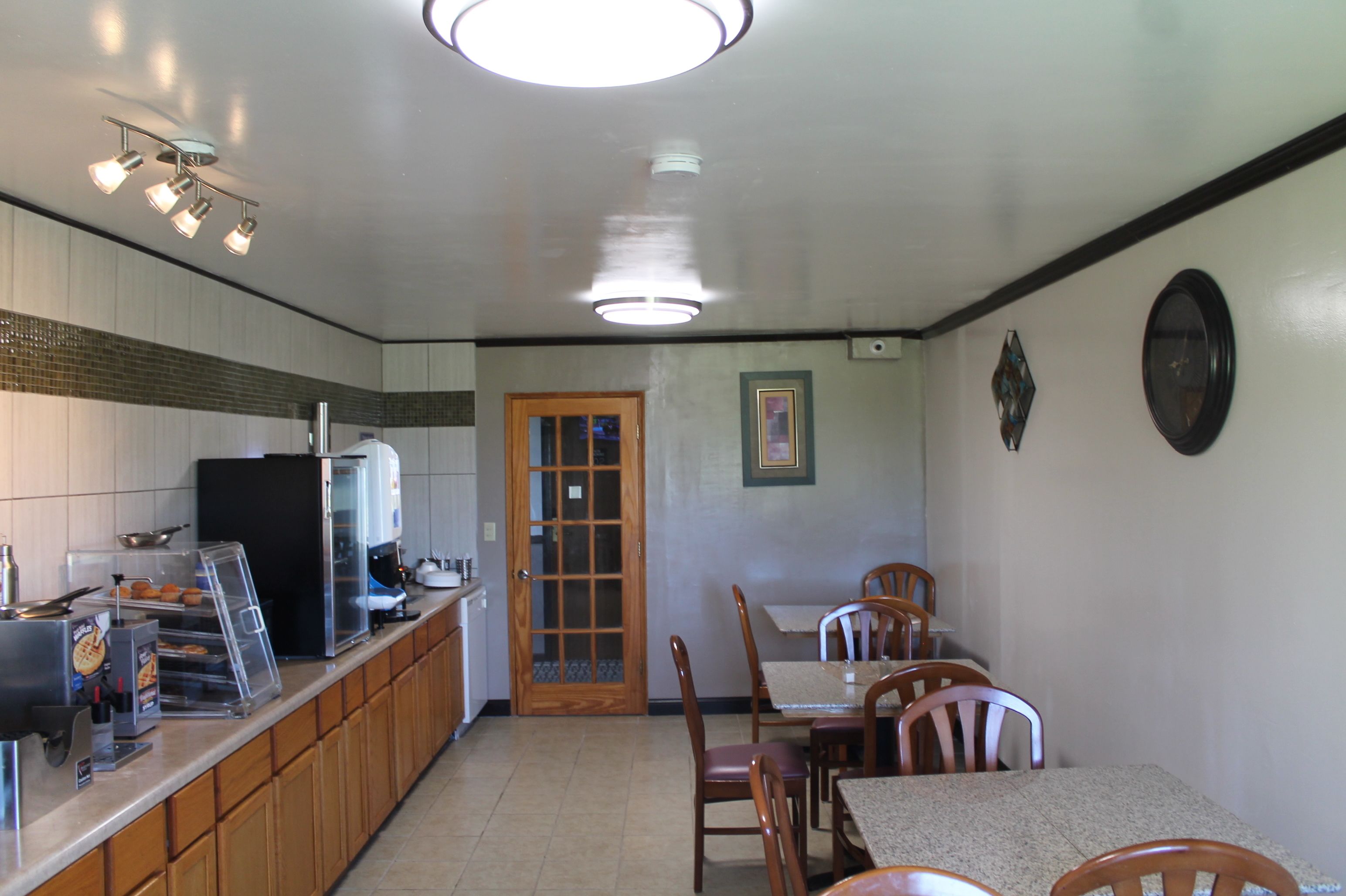 Un petit restaurant propre, avec un comptoir, un réfrigérateur et un espace repas comprenant des chaises en bois et une table.