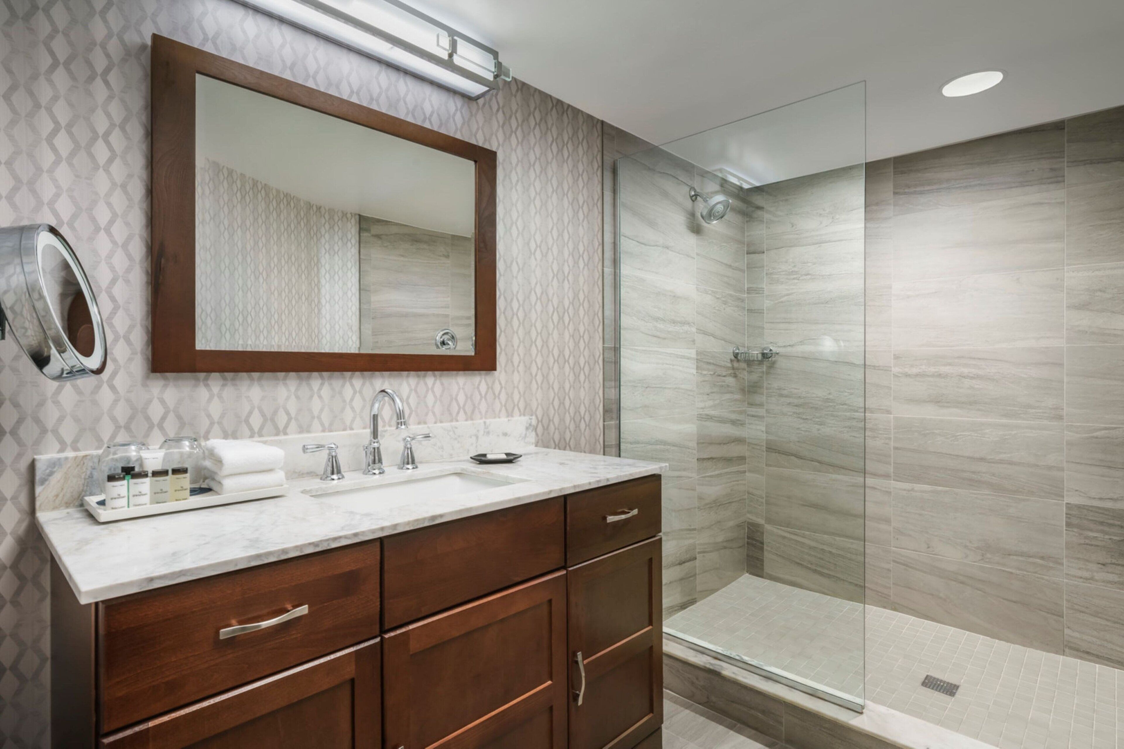 A modern bathroom with a marble vanity, a large mirror, and a glass-enclosed shower.