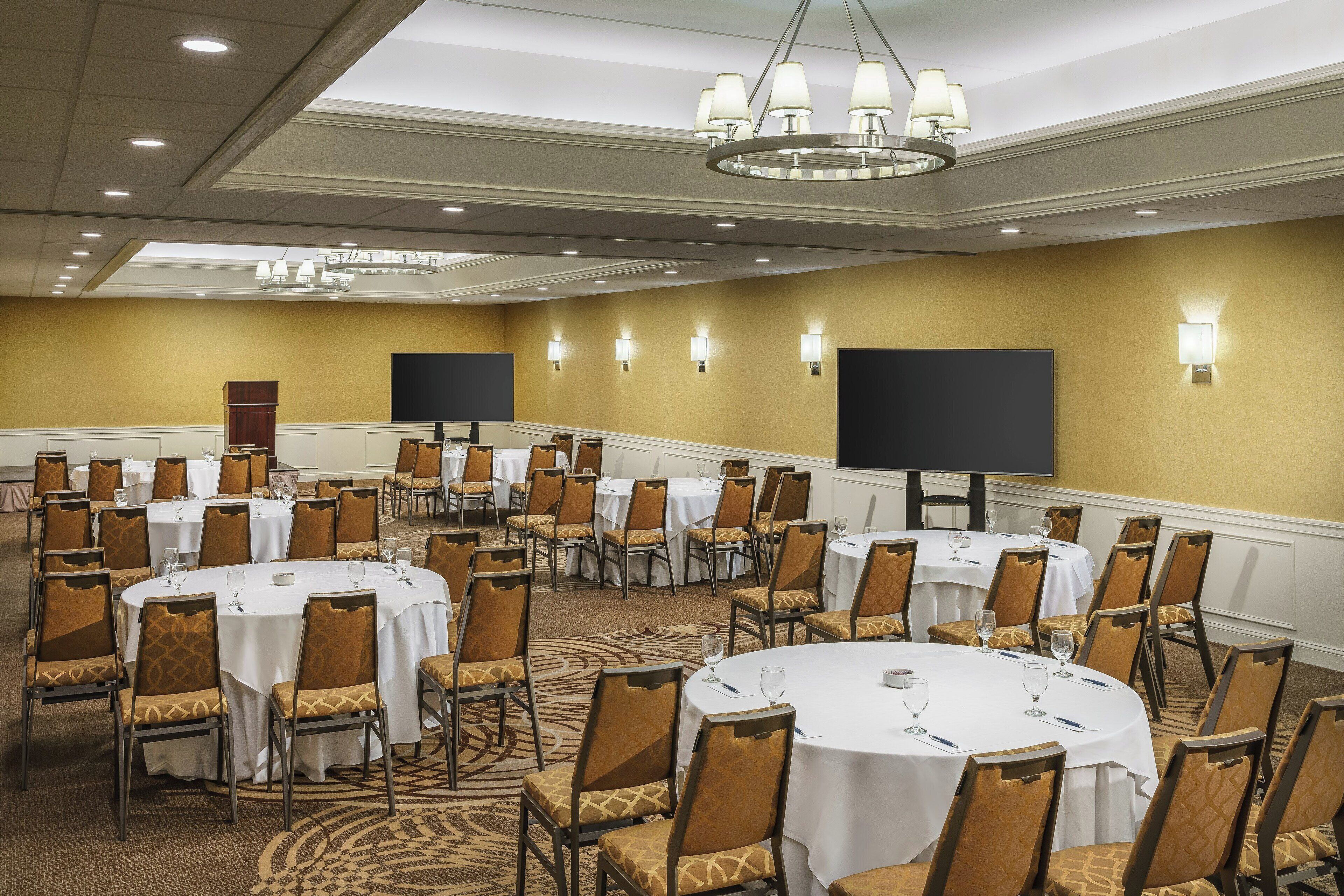 A conference room with multiple round tables, chairs, and a large screen.