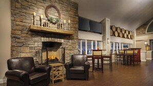 A spacious living area with a stone fireplace, leather armchairs, and a dining area with wooden chairs and a bar. - Sheraton Great Valley Hotel (Malvern)
