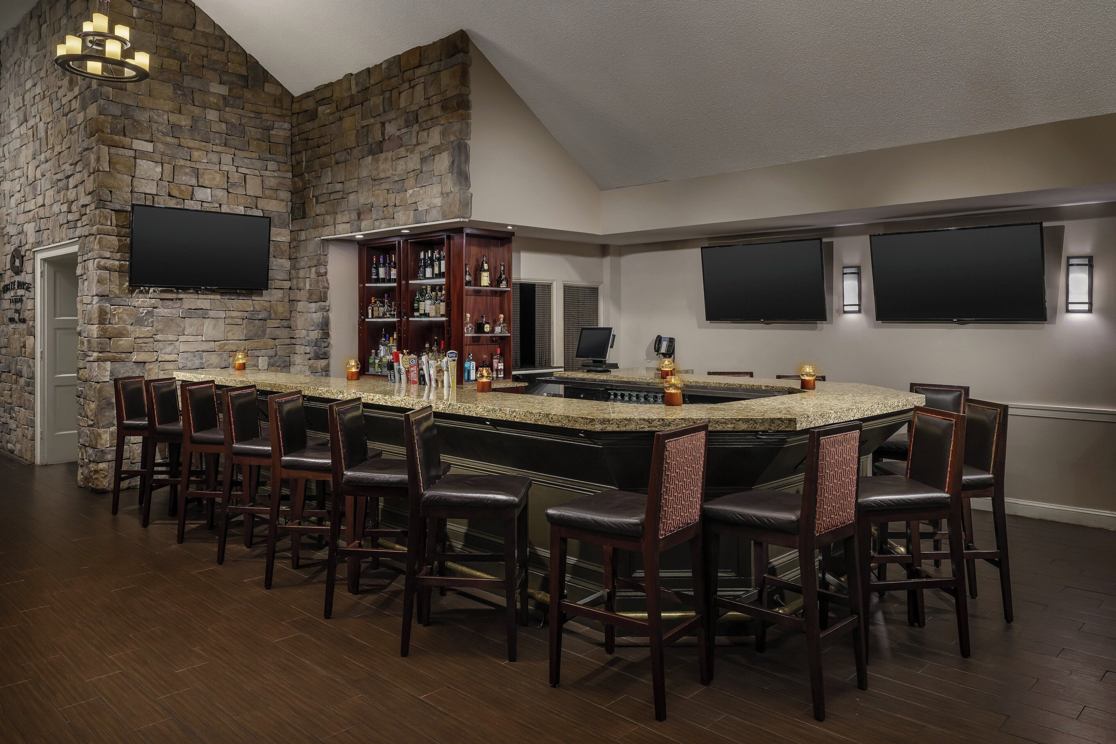 A bar area with a stone wall, multiple TVs, and a bar counter with chairs.