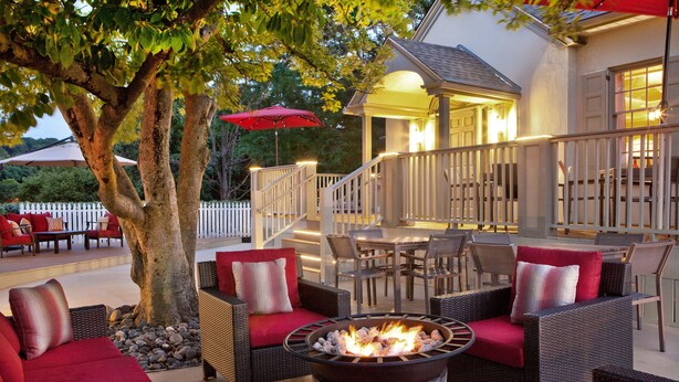 An outdoor patio area with wicker furniture, a fire pit, and a covered seating area with a red umbrella. - Sheraton Great Valley Hotel (Malvern)