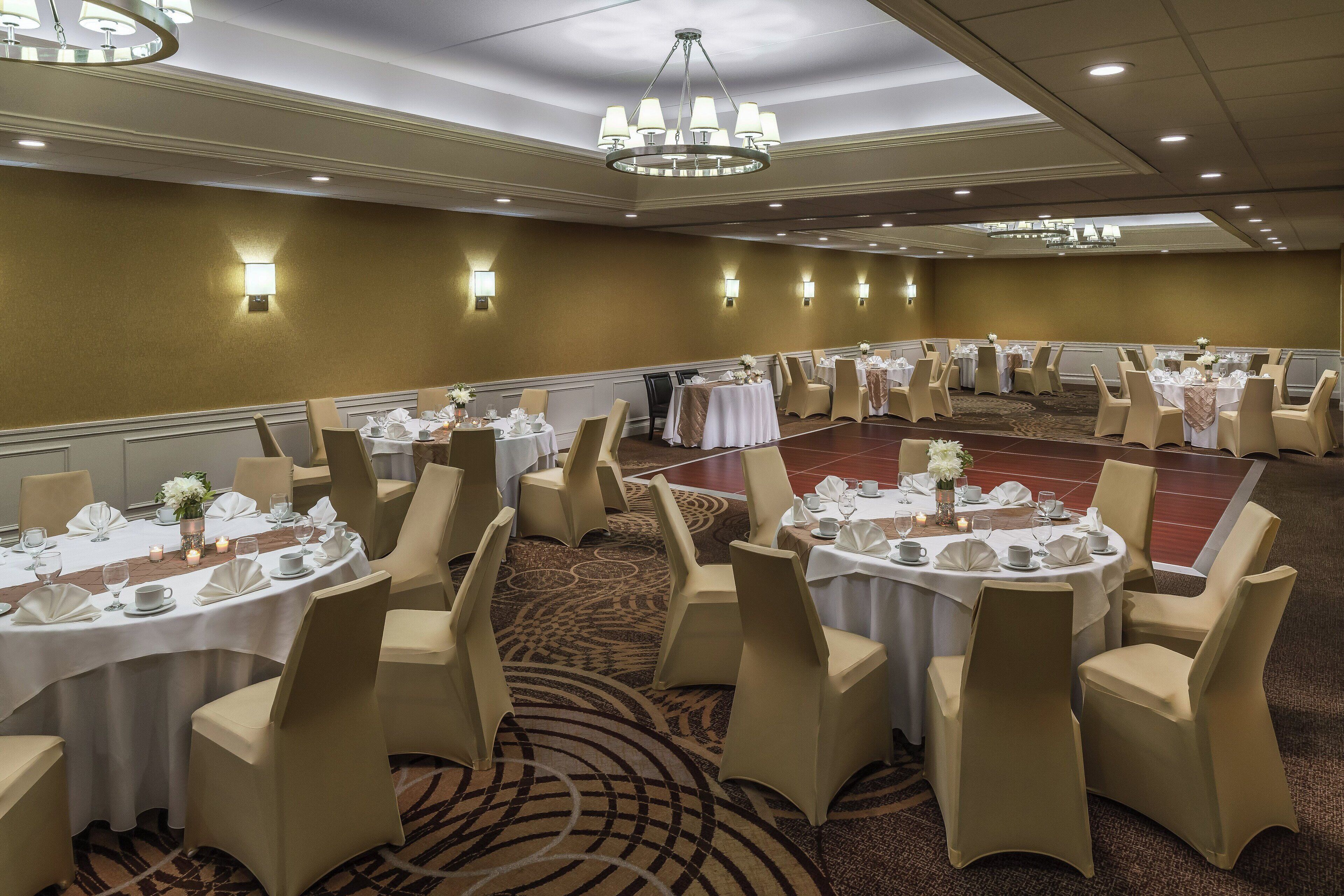 A banquet hall with round tables, beige chairs, and chandeliers.