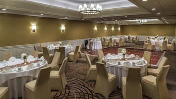 A banquet hall with round tables, beige chairs, and chandeliers.