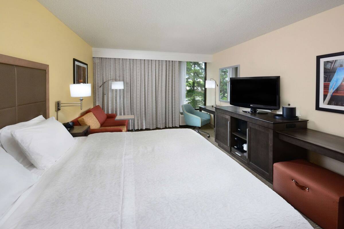 A hotel room with a large bed, a desk with a TV, a chair, and a window with curtains.