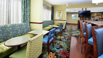 A hotel room with a sofa, chairs, a small table, a TV, and a carpet with a floral pattern.