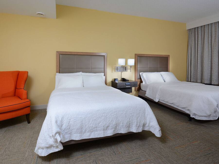 Habitació d'hotel amb dos llits, una tauleta de nit amb làmpades, una cadira i un terra amb moqueta.