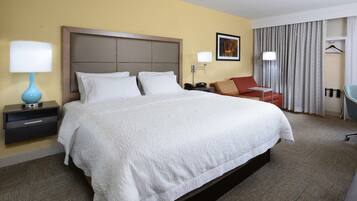 A hotel room with a large bed, a desk, a chair, a lamp, and a wardrobe.