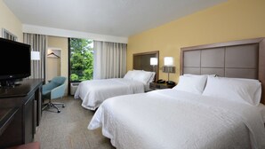 Quarto de hotel com duas camas, uma mesa de trabalho, televisão, uma cadeira e uma janela com cortinas.
