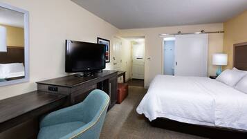 Una camera d'albergo con un letto, una scrivania con televisore, una sedia e un ingresso che conduce a un'altra stanza.