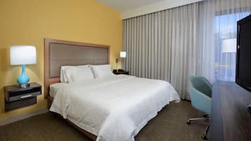 Habitación de hotel con cama, escritorio, silla, televisión y ventana con cortinas.