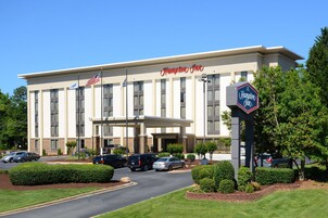 Un hotel Hampton Inn con fachada moderna, una entrada acogedora y un estacionamiento con varios autos.