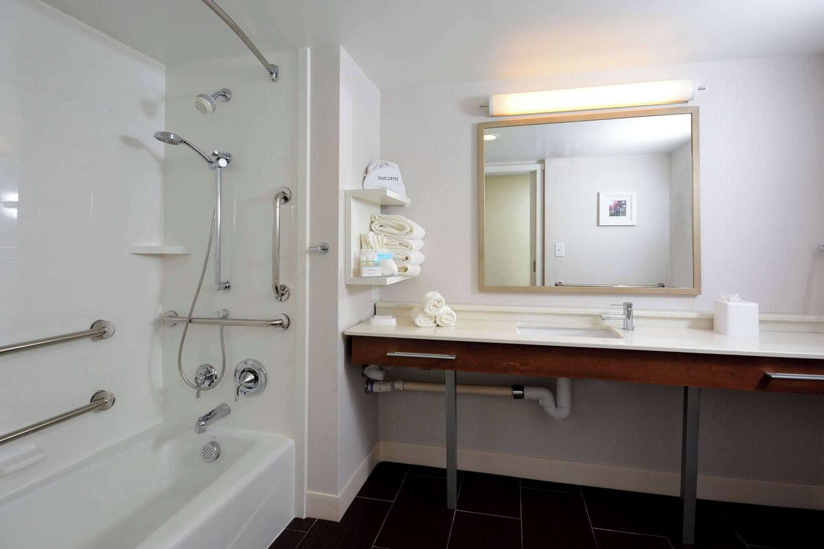 A modern bathroom with a bathtub, a shower, a vanity with a mirror, and a towel rack.