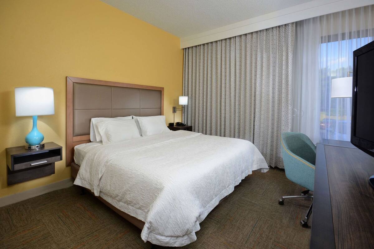 A hotel room with a bed, a desk with a chair, a TV, and a lamp.