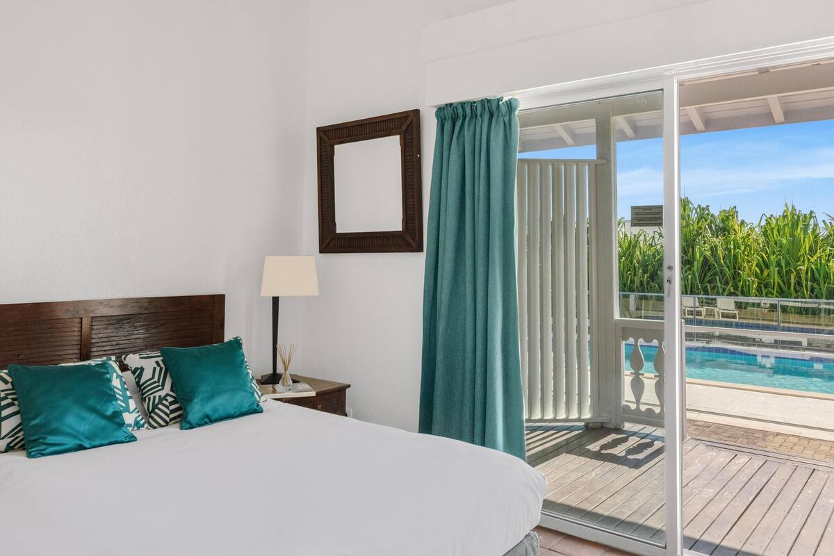 Ein Schlafzimmer mit einem großen Bett, einem Nachttisch, einer Lampe, einem Spiegel und Blick auf einen Swimmingpool.