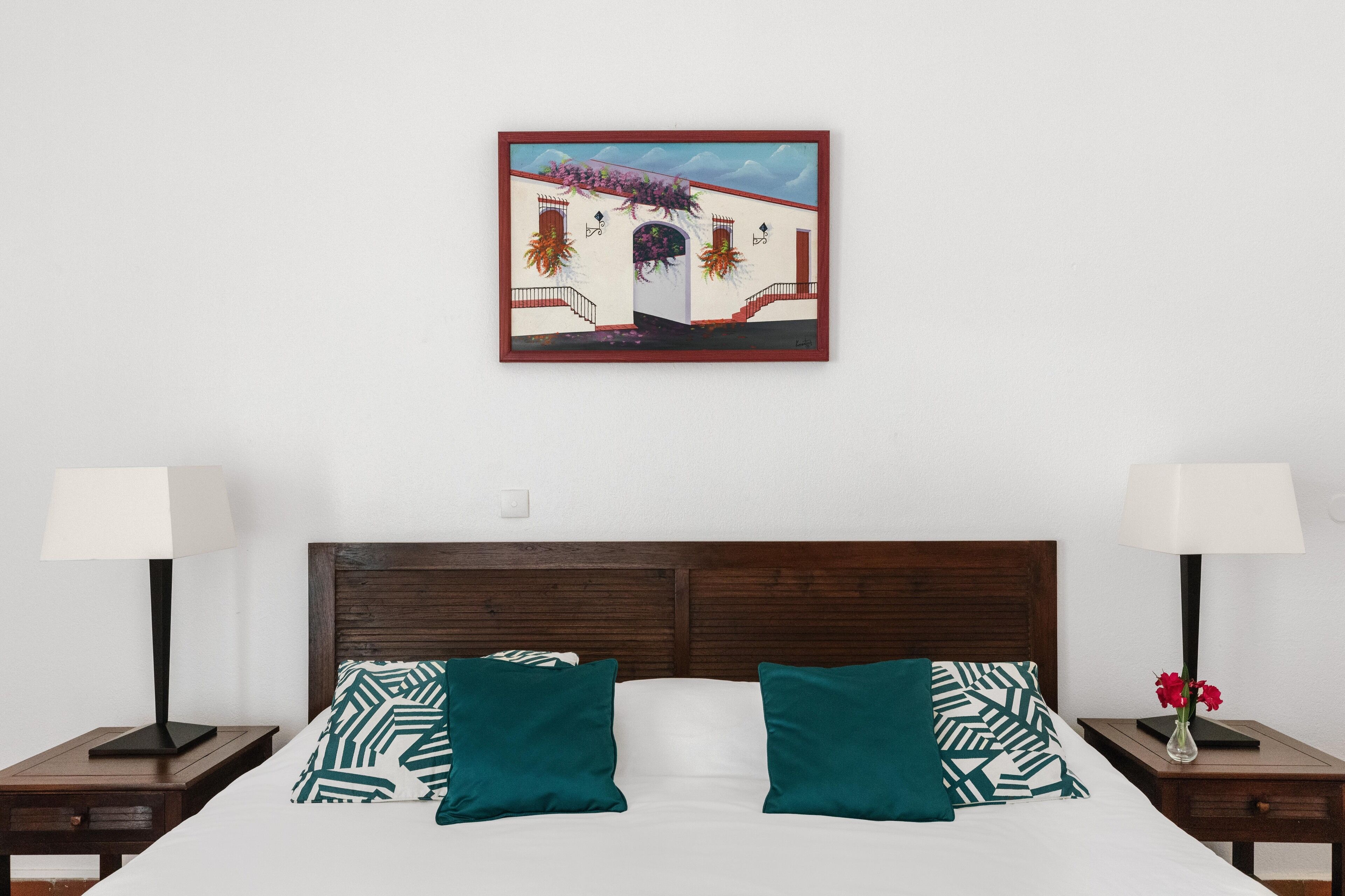 A bedroom with a bed, two nightstands, a framed picture, and a night lamp on each side.