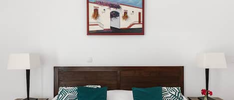 A bedroom with a bed, two nightstands, a framed picture, and a night lamp on each side.