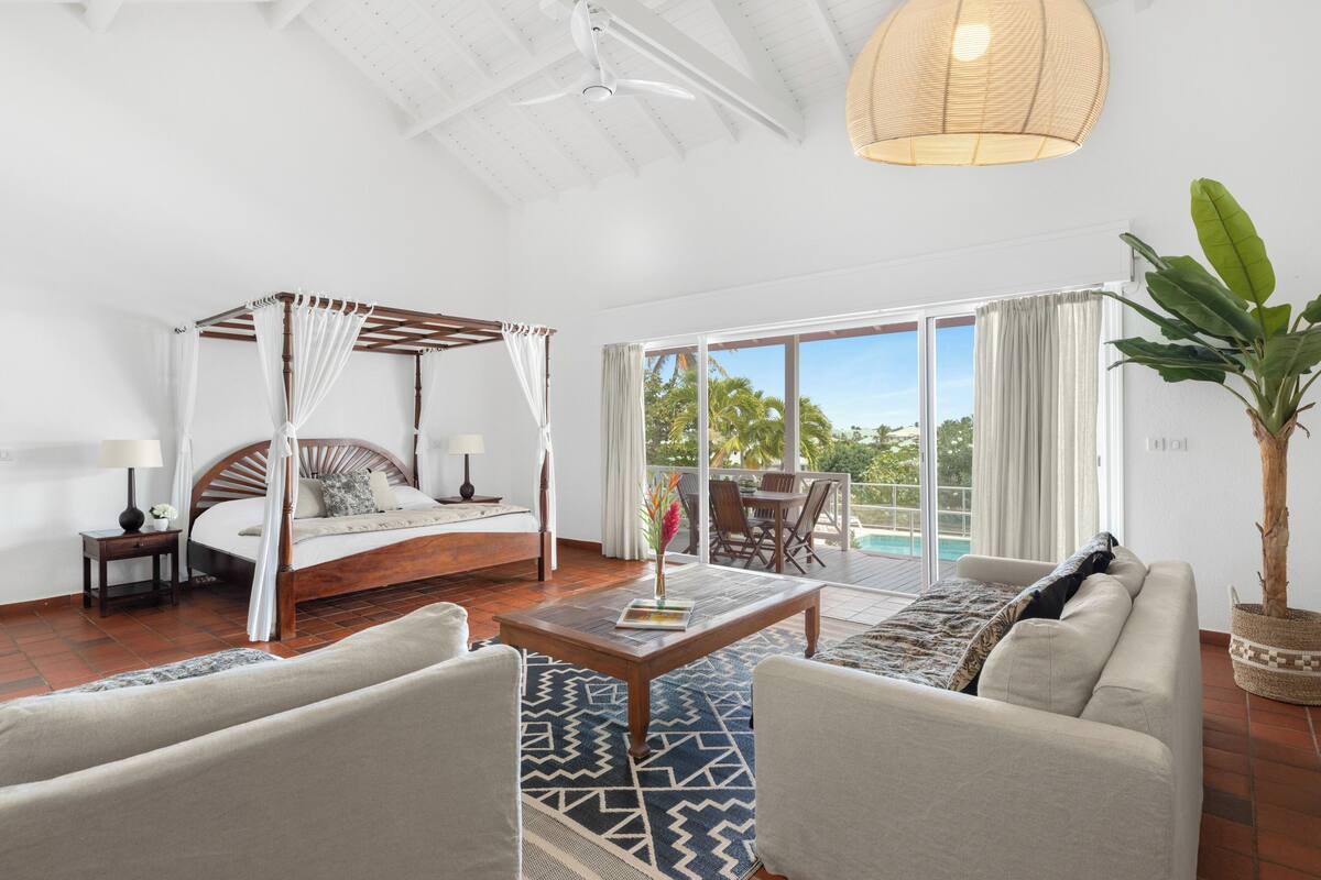 Ein geräumiges Schlafzimmer mit Baldachinbett, einer Sitzecke mit Sofa und Couchtisch sowie Blick auf einen Pool durch große Schiebetüren.