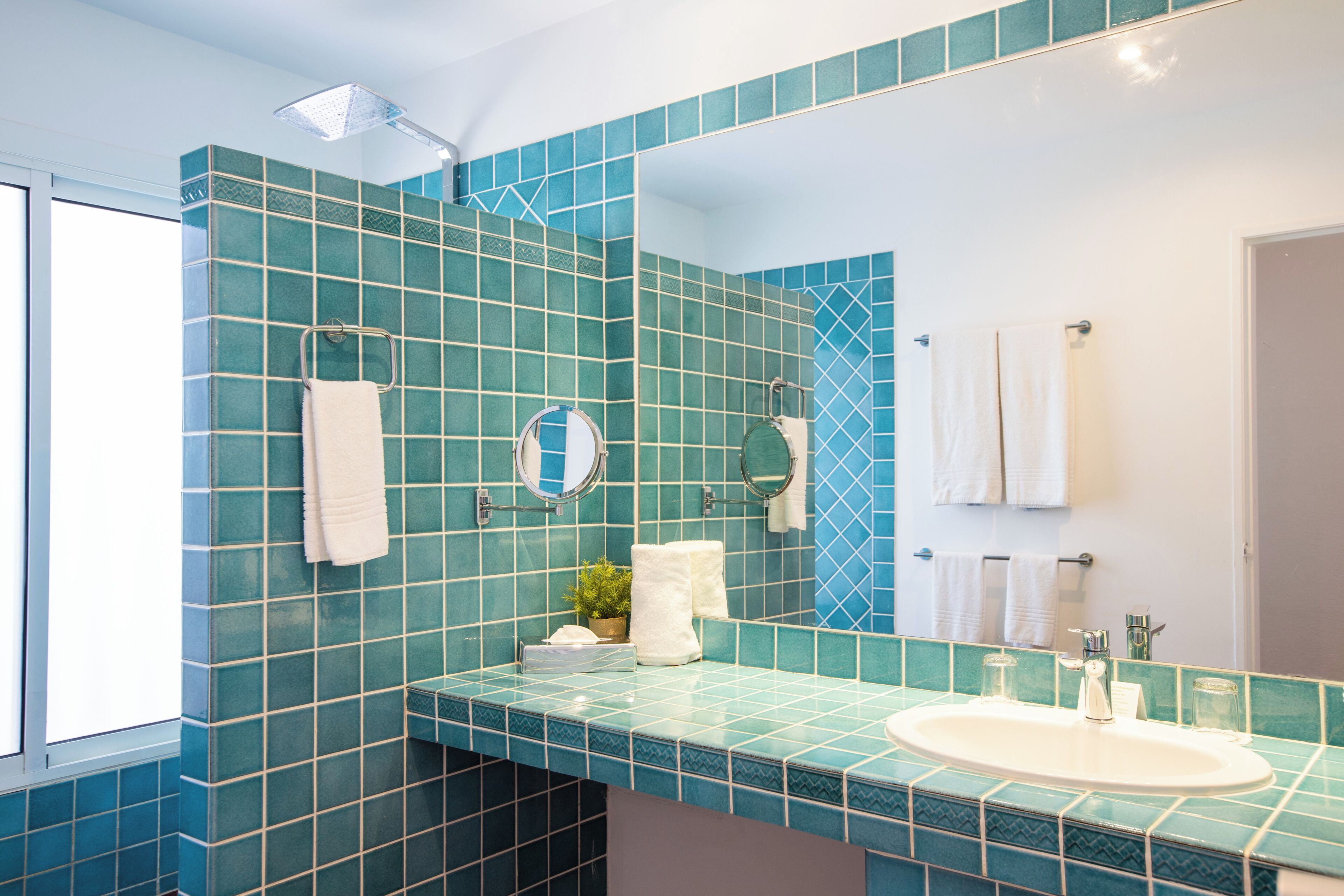 Une salle de bain avec un mur recouvert de carreaux bleus, un lavabo blanc, un miroir et une pomme de douche.