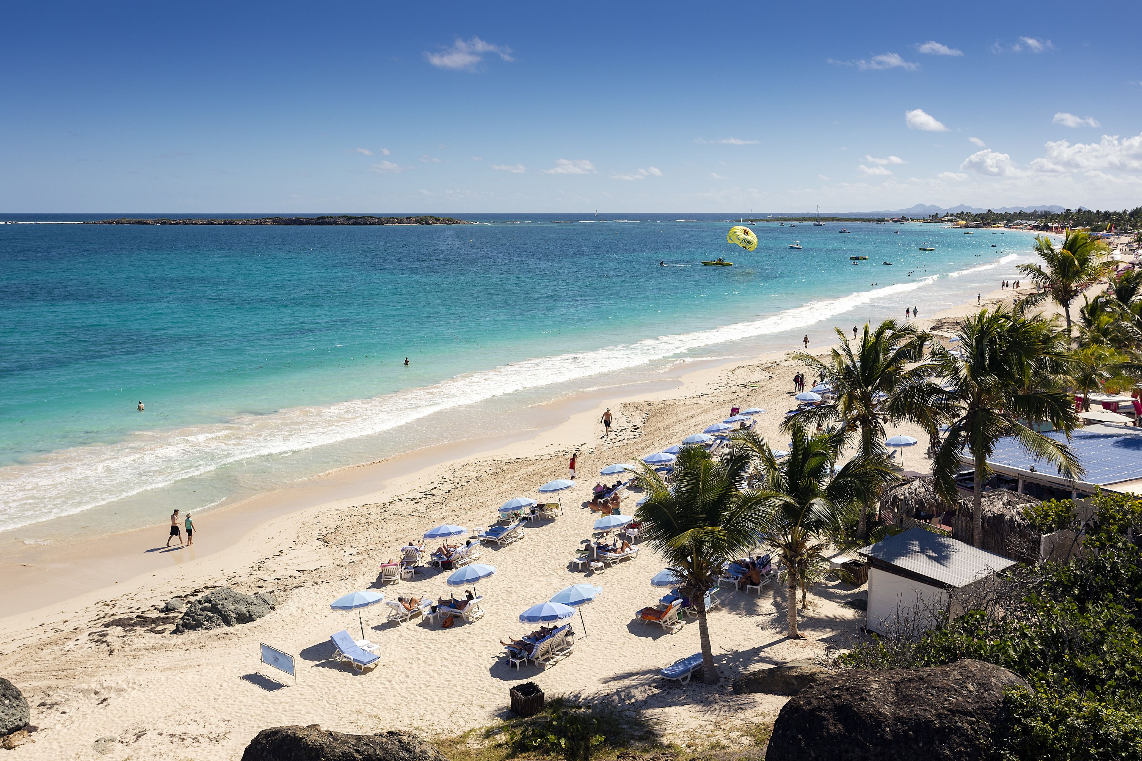 A beach with clear turquoise water, sun loungers, and palm trees.